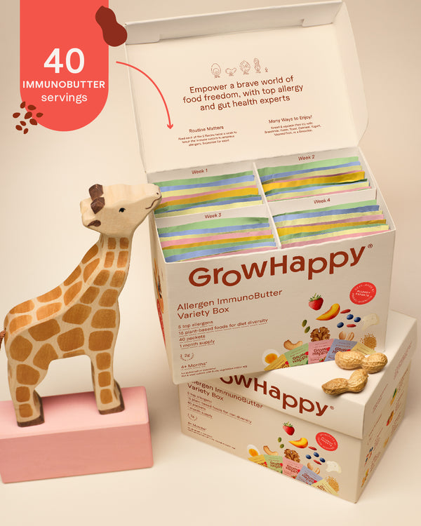 GrowHappy Allergen ImmunoButter Variety Box shown open with multiple colorful butter packets inside, styled on a pink surface with fruit, nuts, and a red callout badge reading 40 immunobutter servings and 5 delicious flavors.